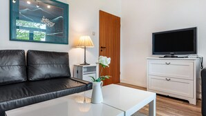 Una sala de estar moderna con un sofá de cuero negro, una mesa de centro blanca, un televisor y una obra de arte enmarcada en la pared.