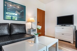A modern living room with a black leather sofa, a white coffee table, a TV, and a framed artwork on the wall. - Apartment '2' with Modern Country-Style Kitchen (Cuxhaven)