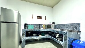 Eine moderne Küche mit einem Edelstahl-Kühlschrank, einer Mikrowelle und einem Spülbecken. Ein blauer Mülleimer und ein dekoratives Wandbild sind ebenfalls vorhanden.