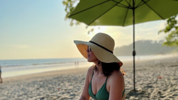 Eine Strandansicht mit einer Person unter einem grünen Sonnenschirm, einem Sandstrand und dem Ozean im Hintergrund.