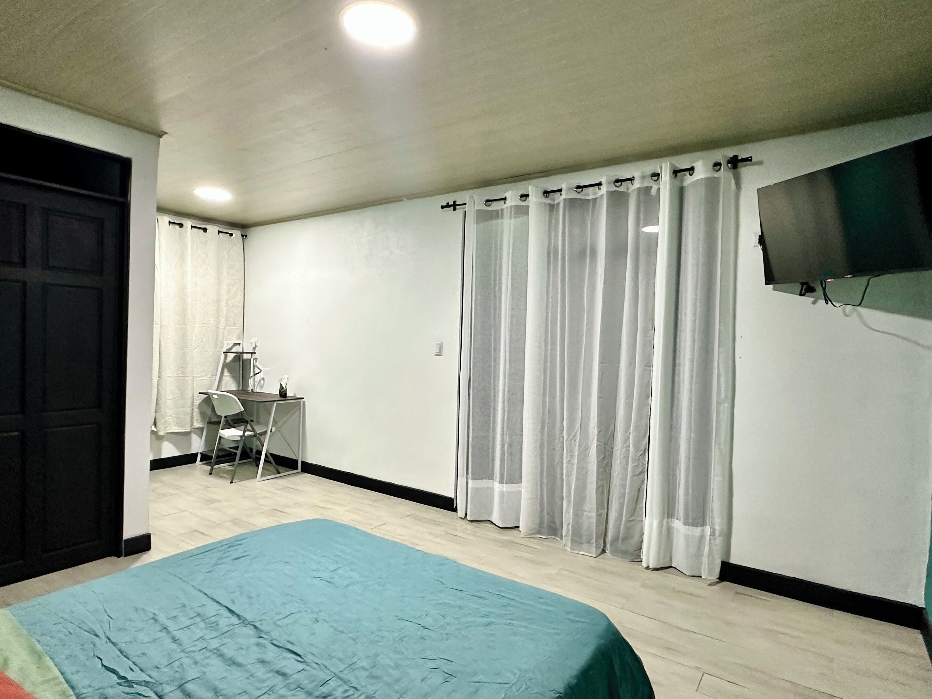 Une chambre à coucher avec un lit, un bureau, une chaise, un téléviseur et une fenêtre avec des rideaux.