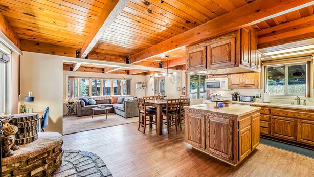 A spacious kitchen with wooden cabinets, a central island, and a dining area with a sofa and chairs. - Cub Cabin Escape: Hot Tub, Games, Fire Pit, BBQ (Big Bear)