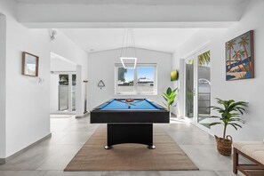 Ein moderner Billardtisch in einem hellen, geräumigen Zimmer mit großem Fenster und Blick ins Freie, gestaltet im minimalistischen Stil.