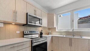 Une cuisine moderne dotée d’appareils électroménagers en acier inoxydable, de meubles de rangement en bois clair et d’une fenêtre laissant entrer la lumière naturelle.