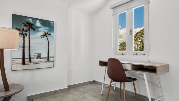 Une pièce comprenant un bureau, une chaise et un tableau représentant des palmiers accroché au mur.