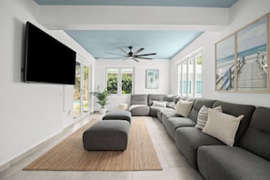 Ein modernes Wohnzimmer mit einem grauen Ecksofa, einem flachbildfernseher an der Wand und einem Deckenventilator.