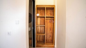 A wooden wardrobe with multiple shelves and hanging space, located in a hallway with a white wall and a door leading to another room. - Sundari Guesthouse Pererenan (Pererenan)