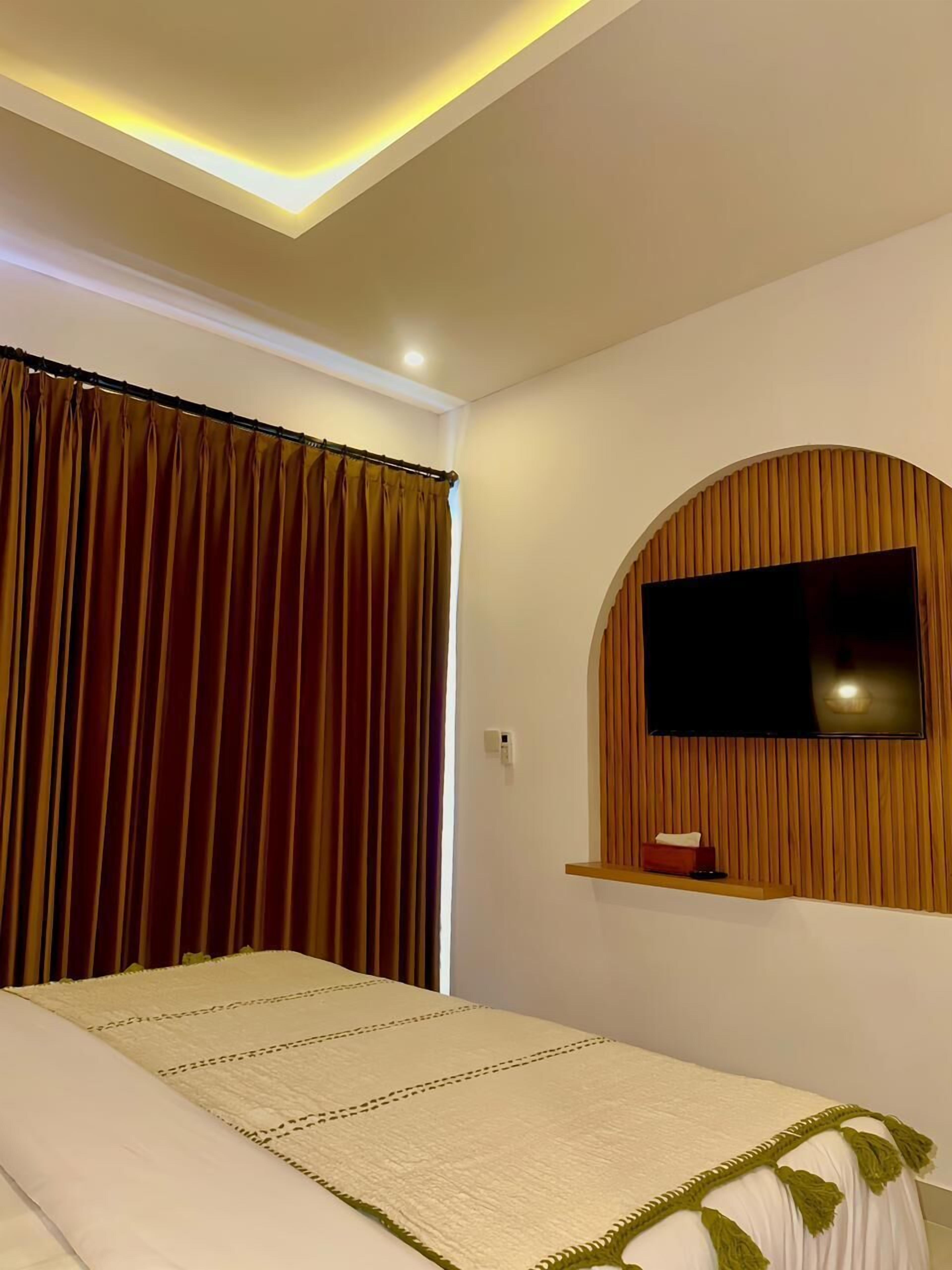 Une chambre d’hôtel avec un lit, un téléviseur fixé au mur, qui est recouvert d’un panneau en bois, et un rideau.