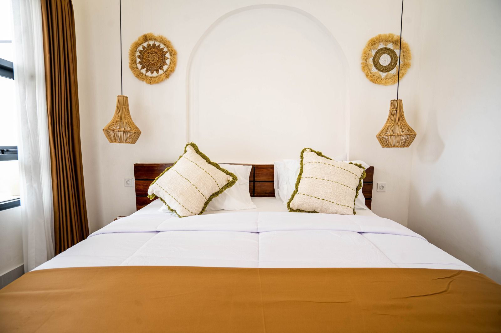 A neatly made bed with two pillows, a brown bedspread, and two wall-mounted lamps.