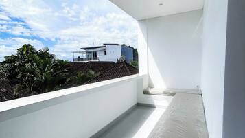 Ein moderner, minimalistischer Raum mit großem Fenster und Blick auf eine Wohngegend. Das Zimmer verfügt über eine weiße Decke, ein kleines Bett mit Matratze und eine weiße Wand.