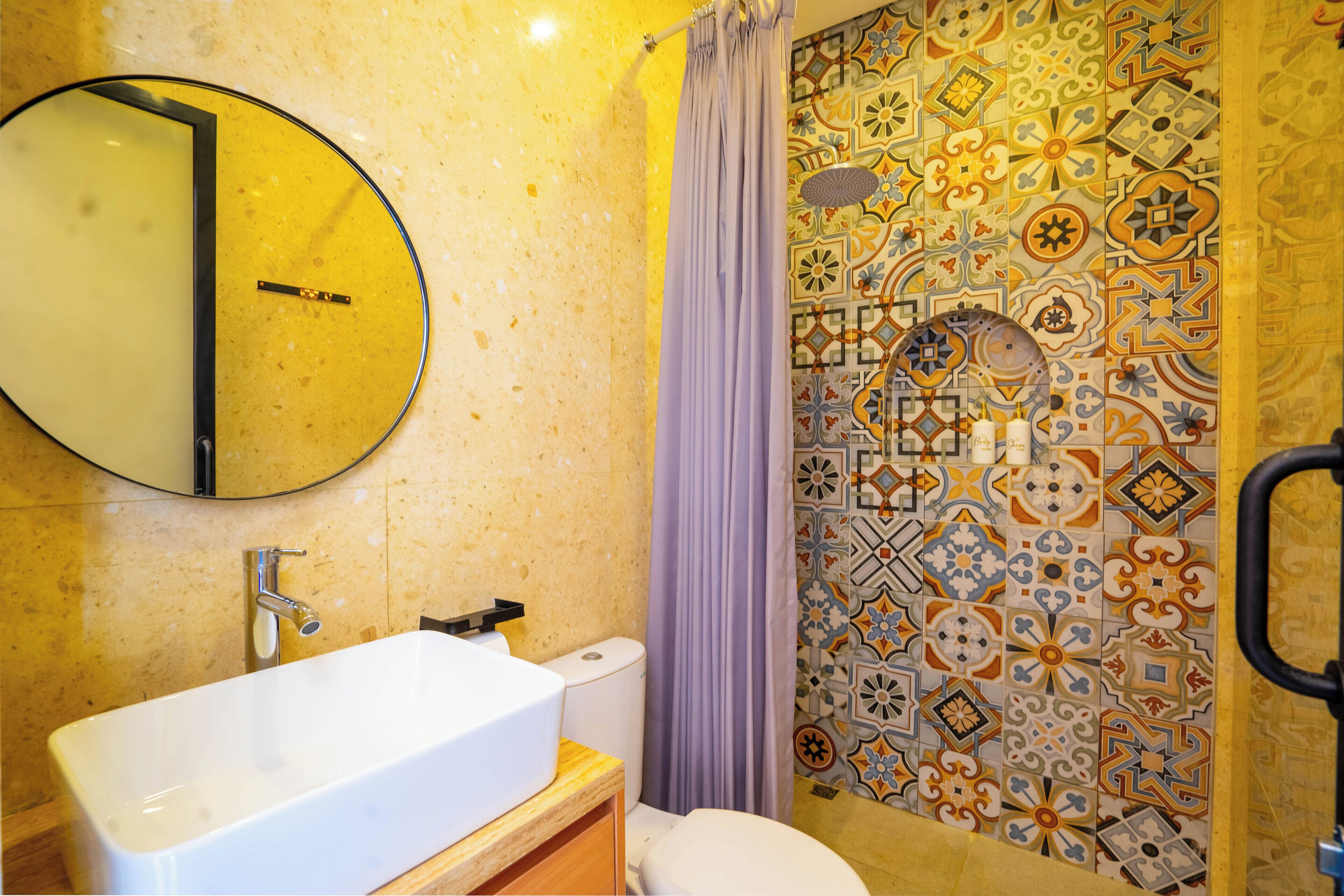 A bathroom with a white sink, a mirror, a toilet, and a shower with a patterned tile wall.