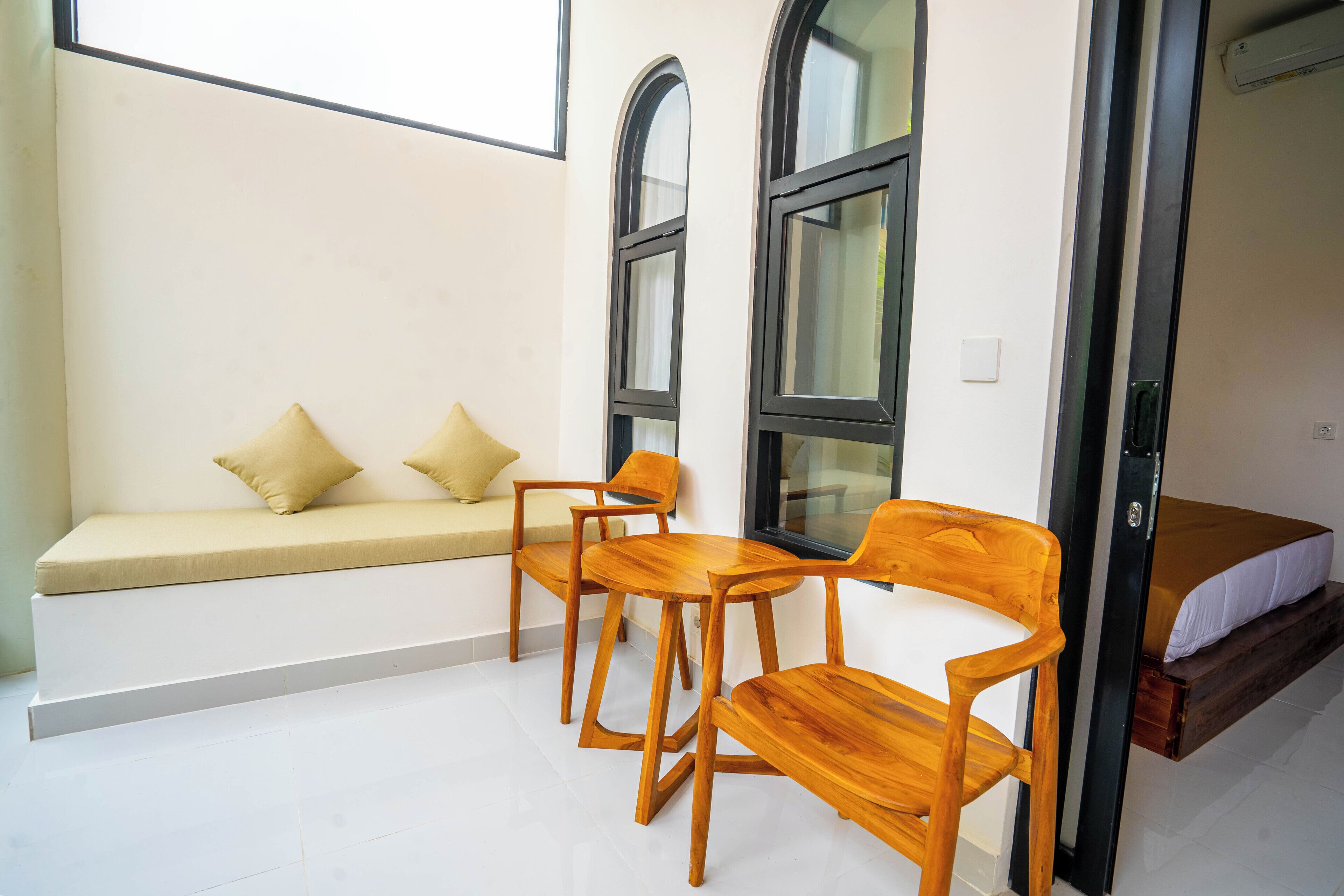 A room with a sofa, two wooden chairs, a small table, and a bed.