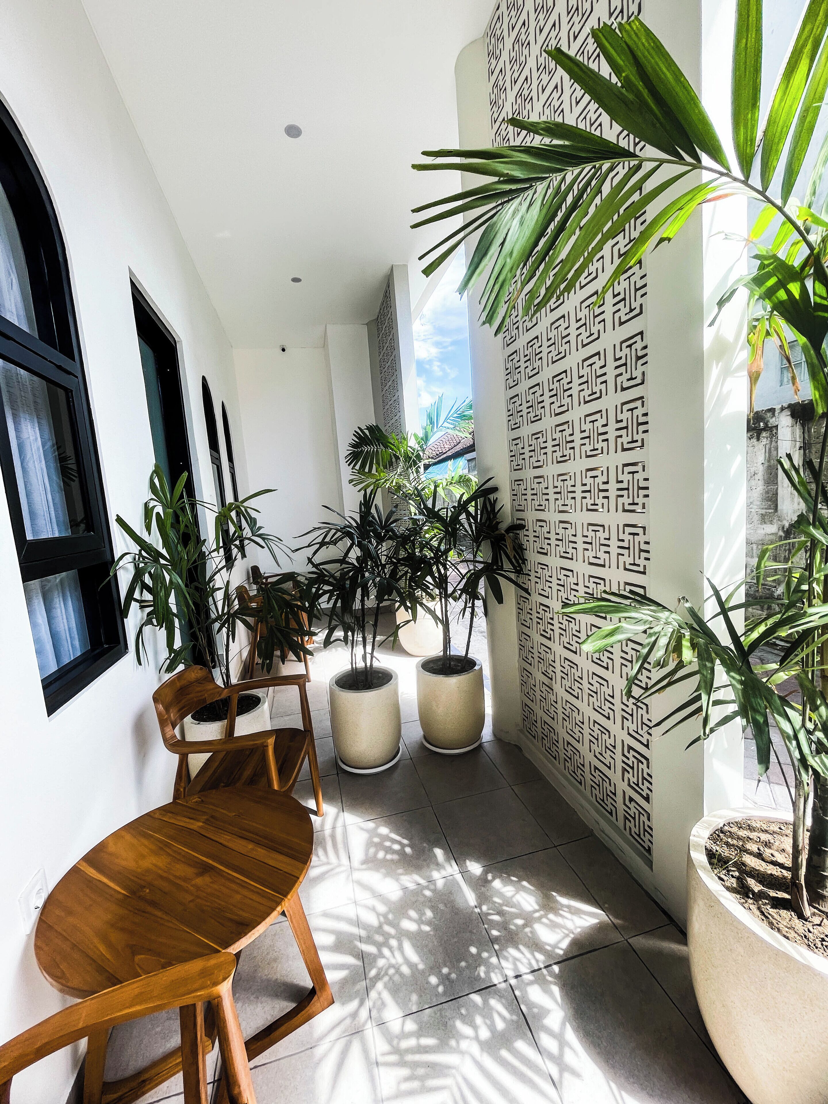 A narrow indoor corridor with potted plants, a wooden chair, and a tiled floor.