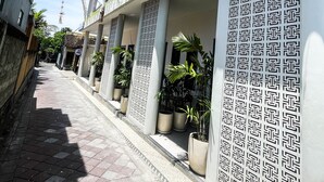 A narrow street with a row of white buildings featuring arched windows and columns, potted plants, and a patterned wall design. - Sundari Guesthouse Pererenan (Pererenan)