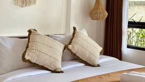 A bed with two pillows, a macrame wall hanging, a woven wall hanging, and a hanging light fixture. - Sundari Guesthouse Pererenan (Pererenan)