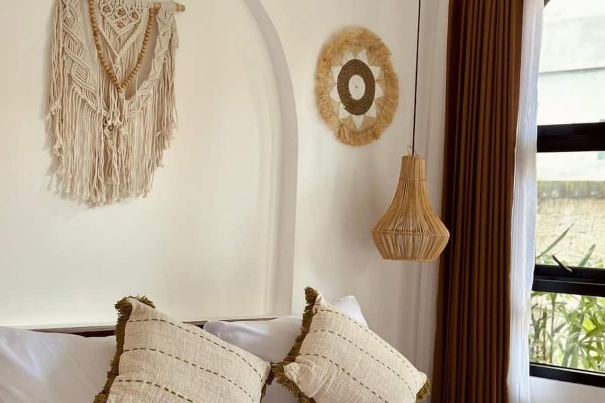Ein Bett mit zwei Kissen, einer Wandbehang aus Makramee, einem gewebten Wandbild und einer Pendelleuchte.
