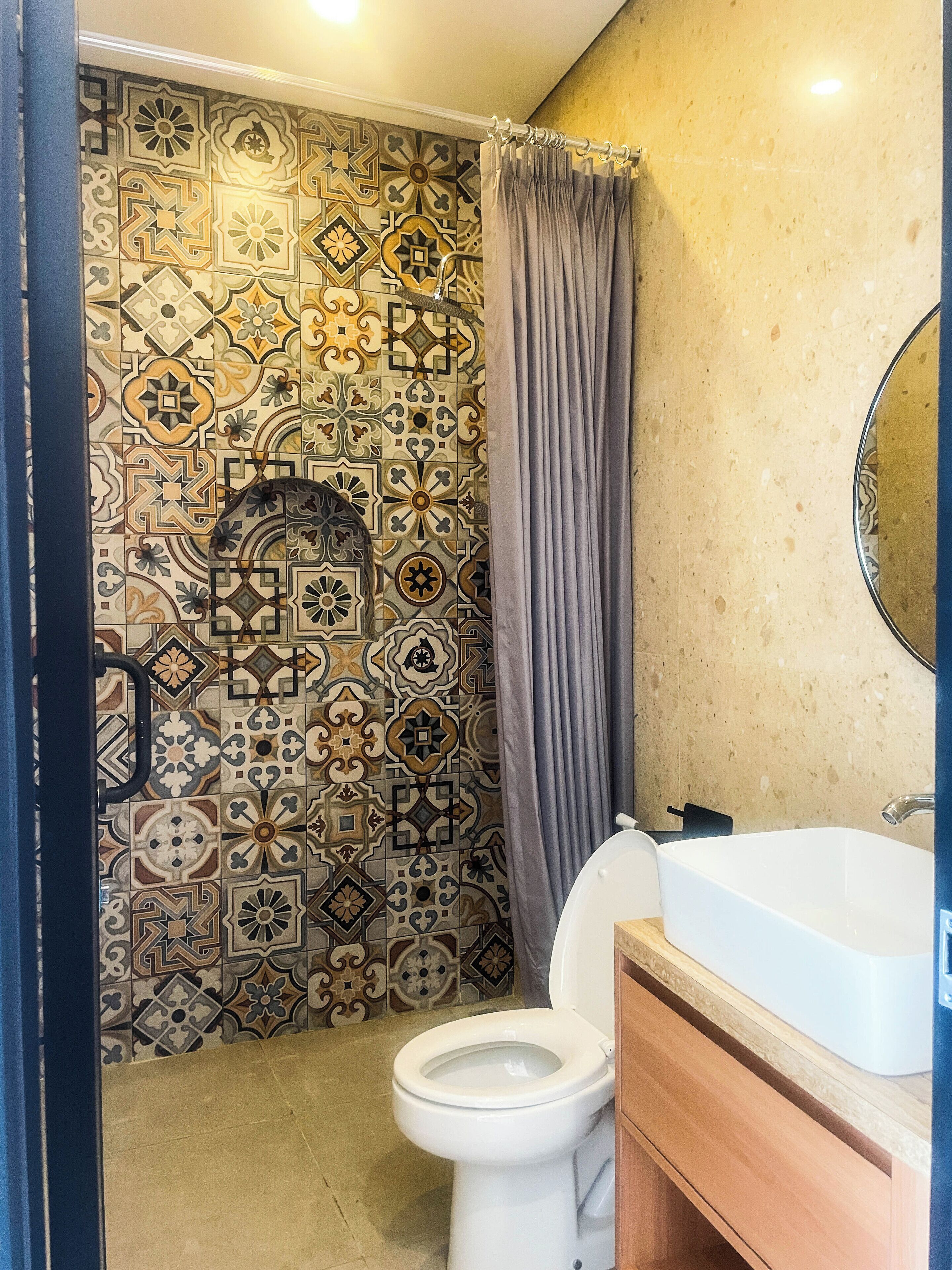 A bathroom with a patterned tile wall, a toilet, a sink, and a mirror.