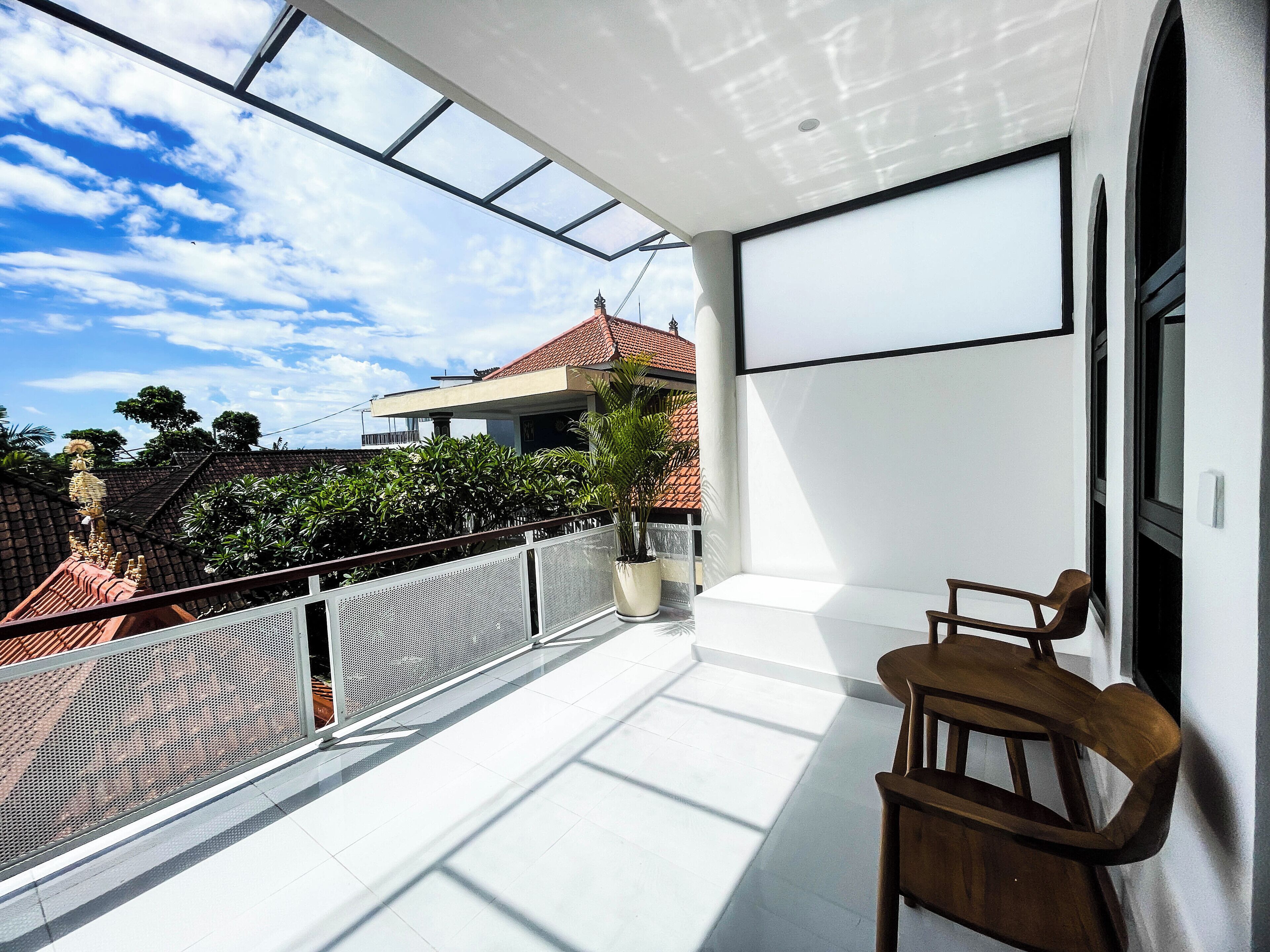 Un balcon donnant sur un immeuble aux toits rouges, avec une plante en pot et une chaise en bois.
