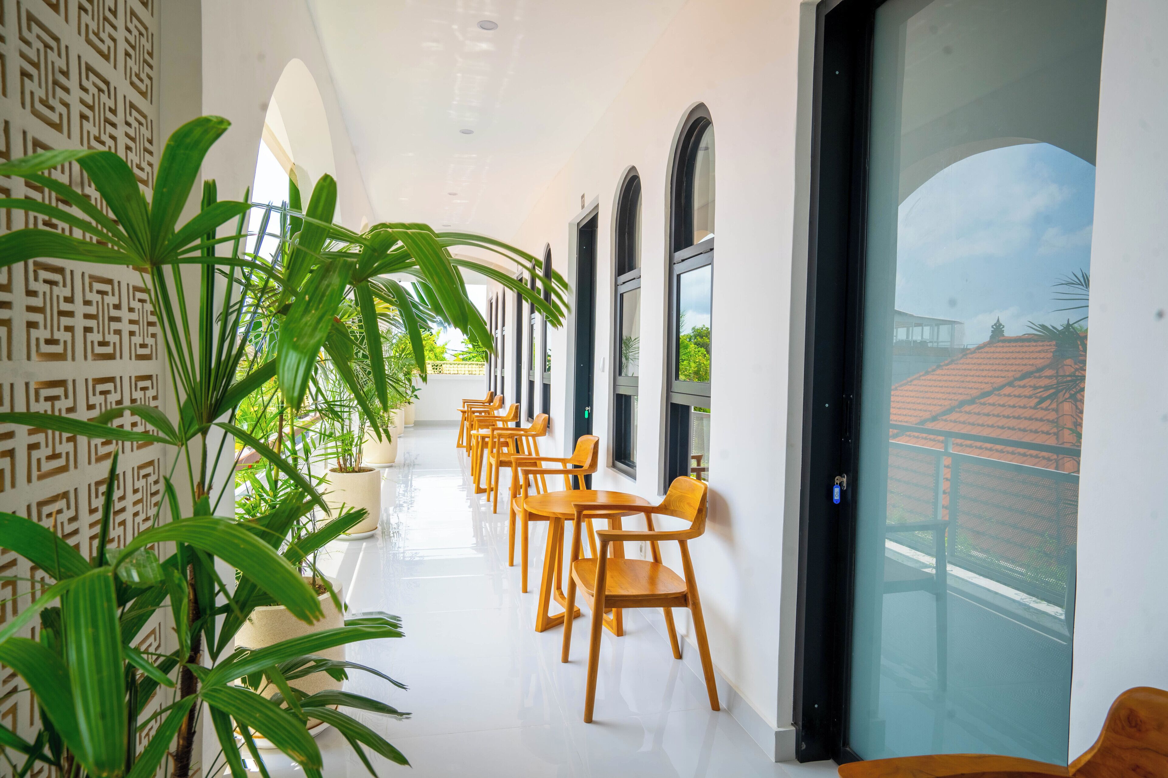 A corridor with potted plants, wooden chairs, and a glass door leading outside.