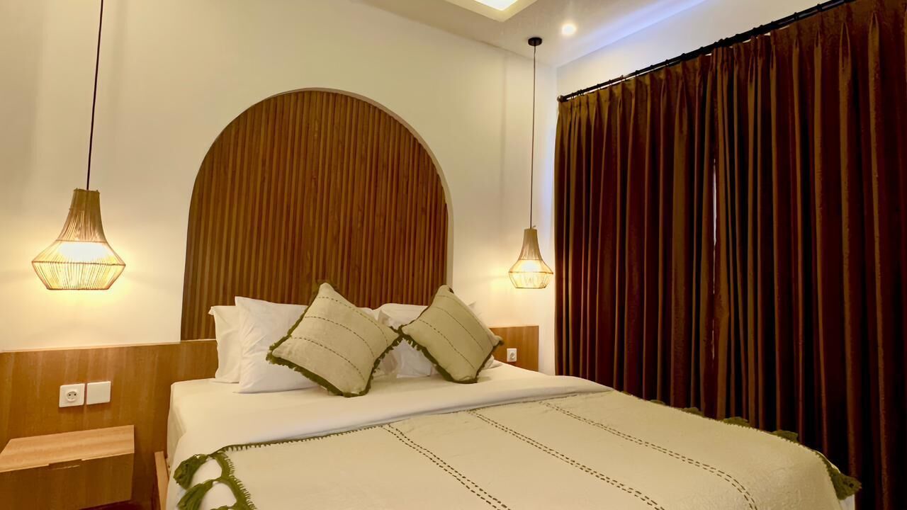 A neatly made bed with a headboard, two bedside lamps, and a curtain on the window.