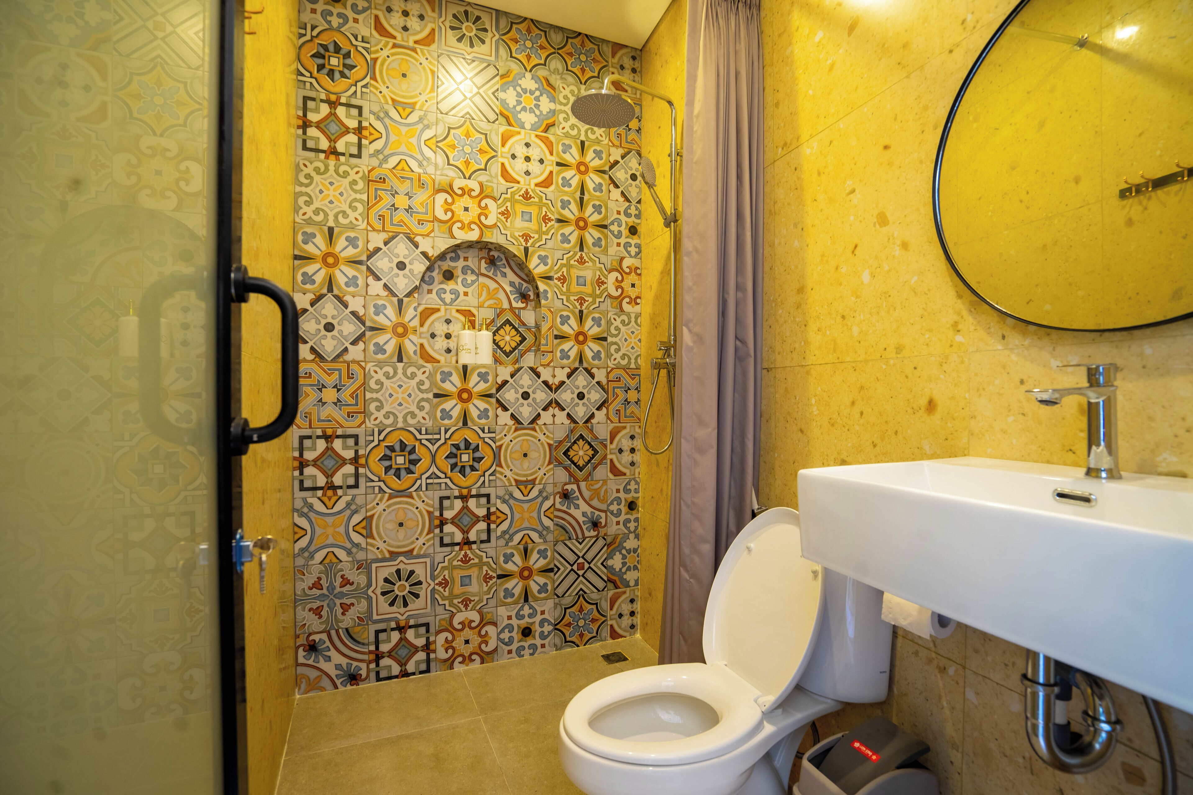 Un baño con inodoro blanco, lavabo y zona de ducha con pared de azulejos estampados.