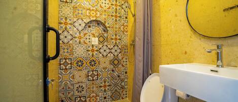 Un baño con inodoro blanco, lavabo y zona de ducha con pared de azulejos estampados.