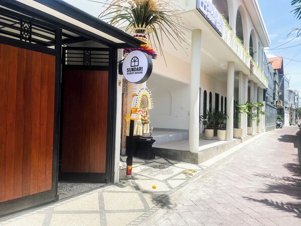 A guest house with a wooden door, a sign reading "SUNDARI GUEST HOUSE", and a decorative archway with a floral arrangement. - Sundari Guesthouse Pererenan (Pererenan)
