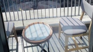 Un balcon doté d’une table en verre et de deux chaises, offrant une vue sur un paysage urbain avec différents bâtiments.