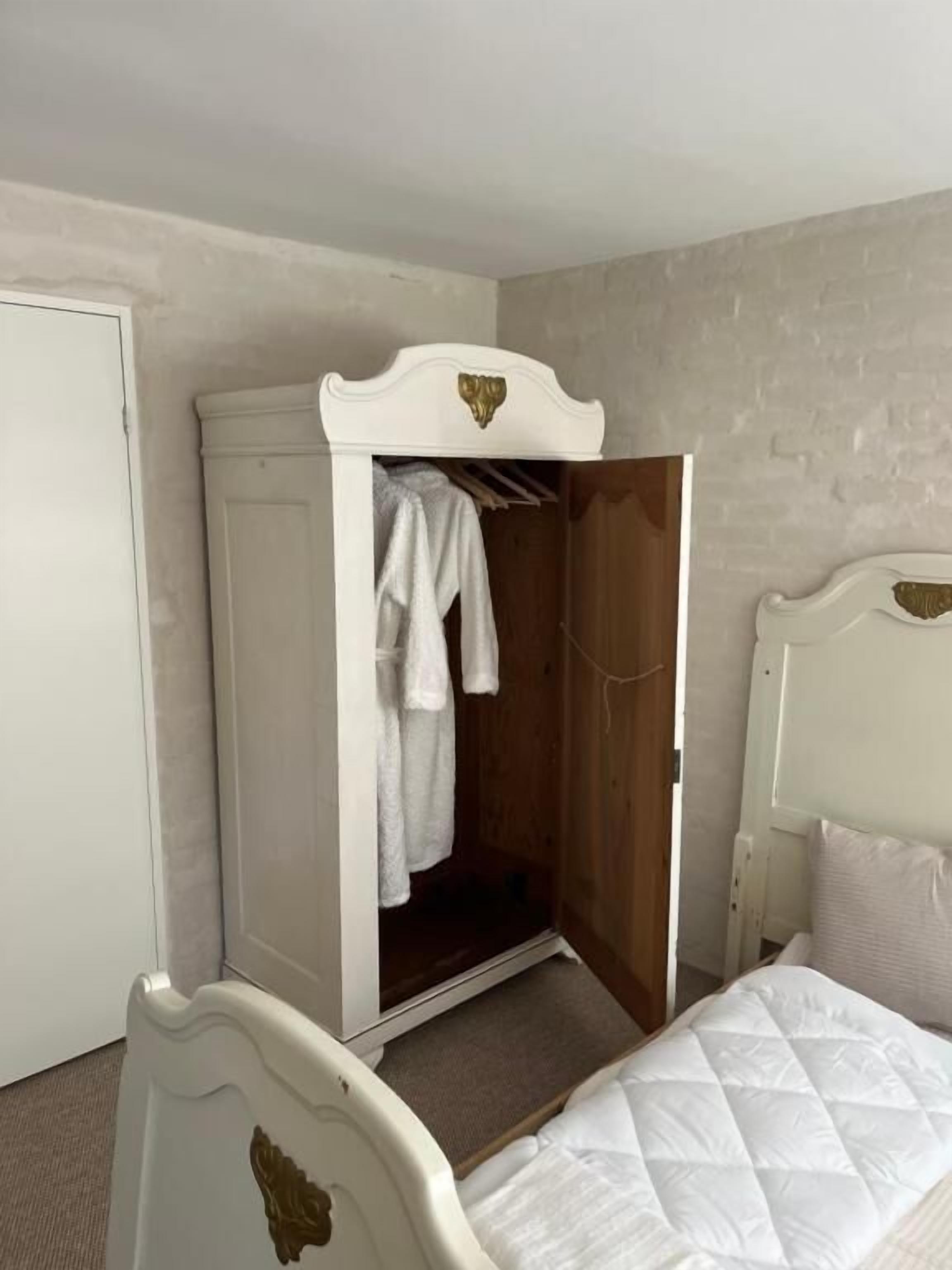 A bedroom with a white wardrobe, a bed with a quilted mattress, and a wooden headboard.