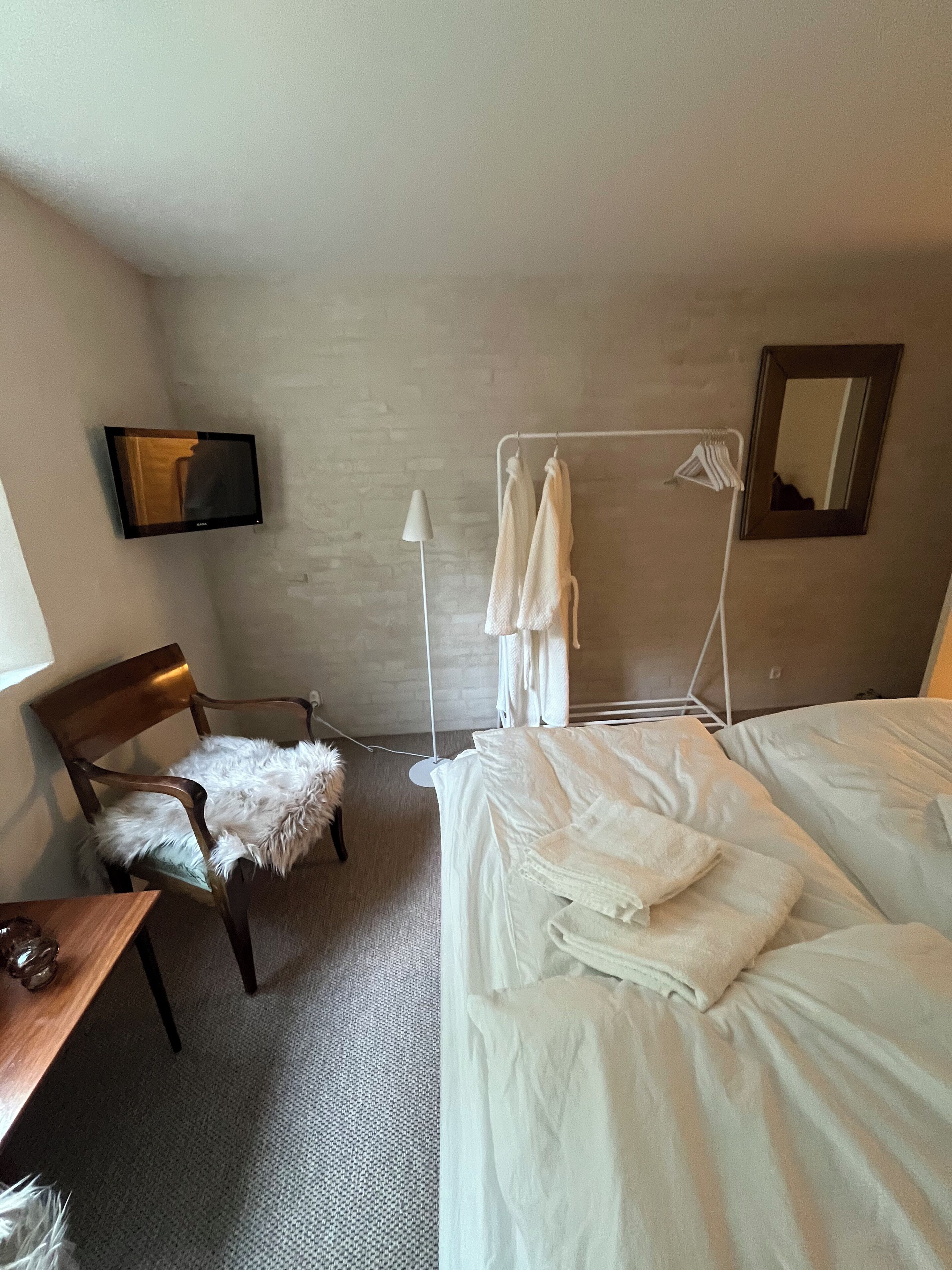 A room with two beds, a chair with a fur throw, a hanging towel rack, and a mirror on the wall.