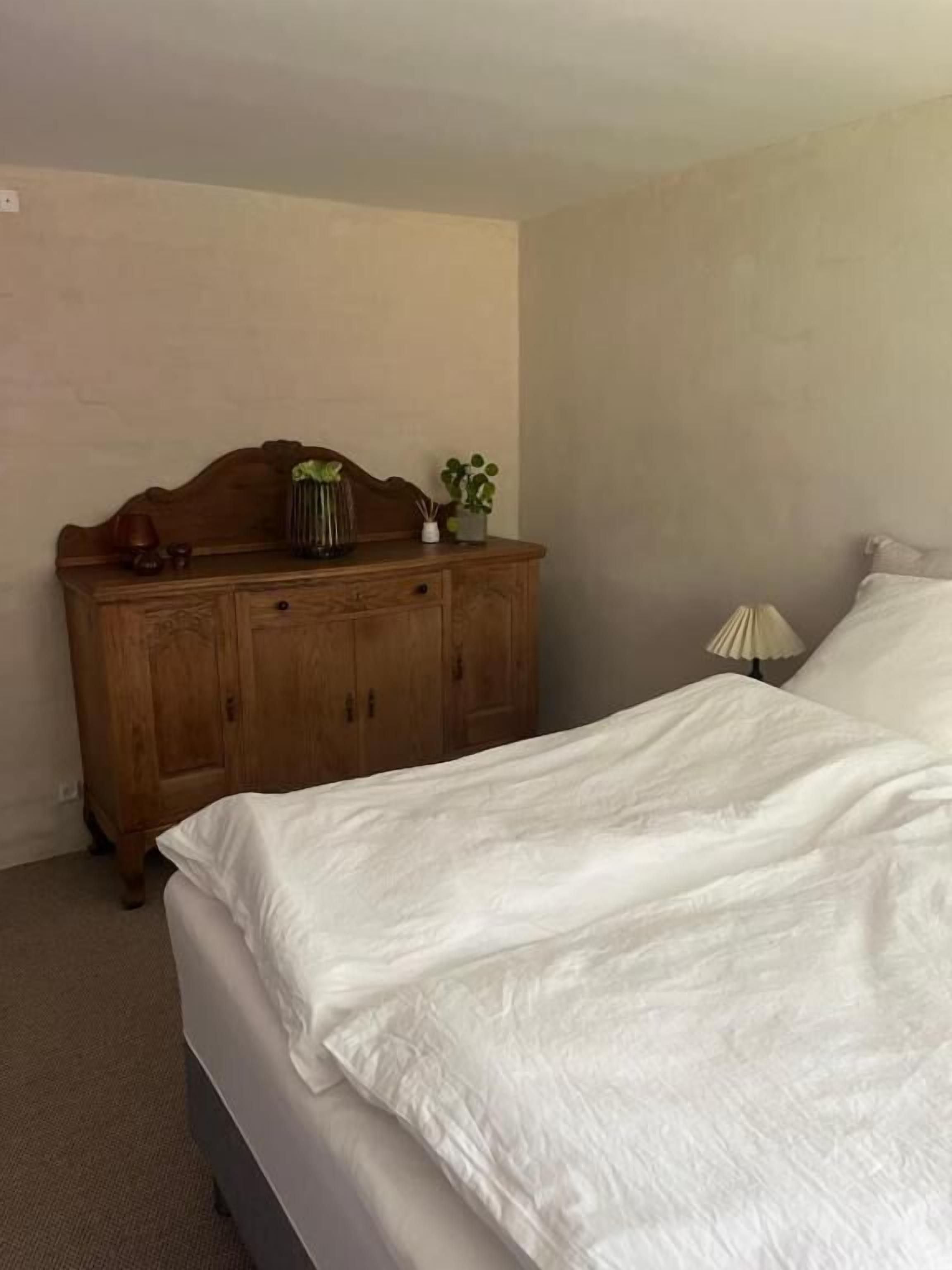 A bedroom with a bed, a wooden dresser, and a lamp.