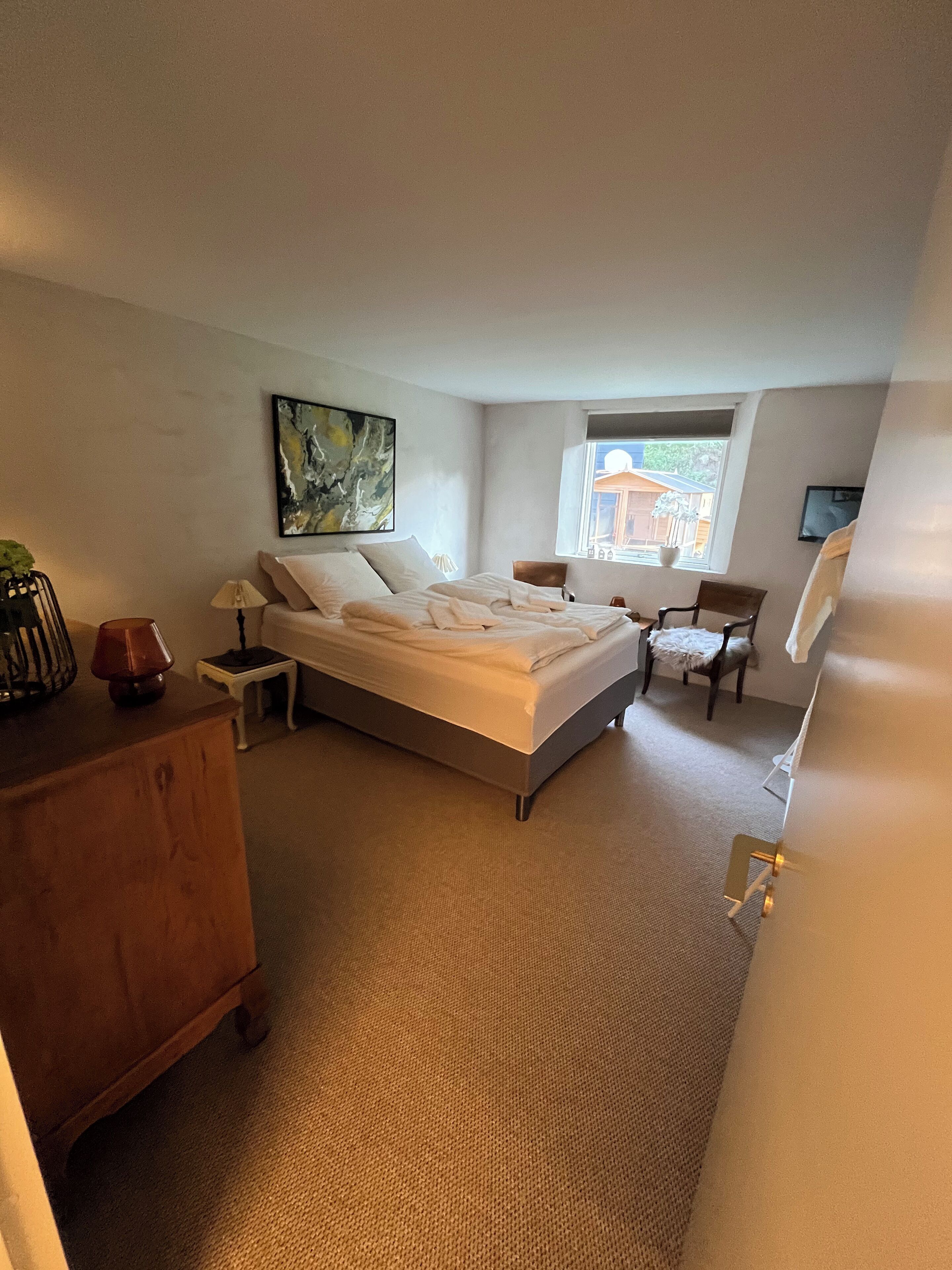 A bedroom with a bed, a nightstand, a dresser, a chair, a window, and a painting on the wall.