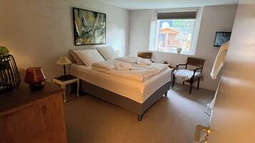 A bedroom with a bed, a nightstand, a dresser, a chair, a window, and a painting on the wall.