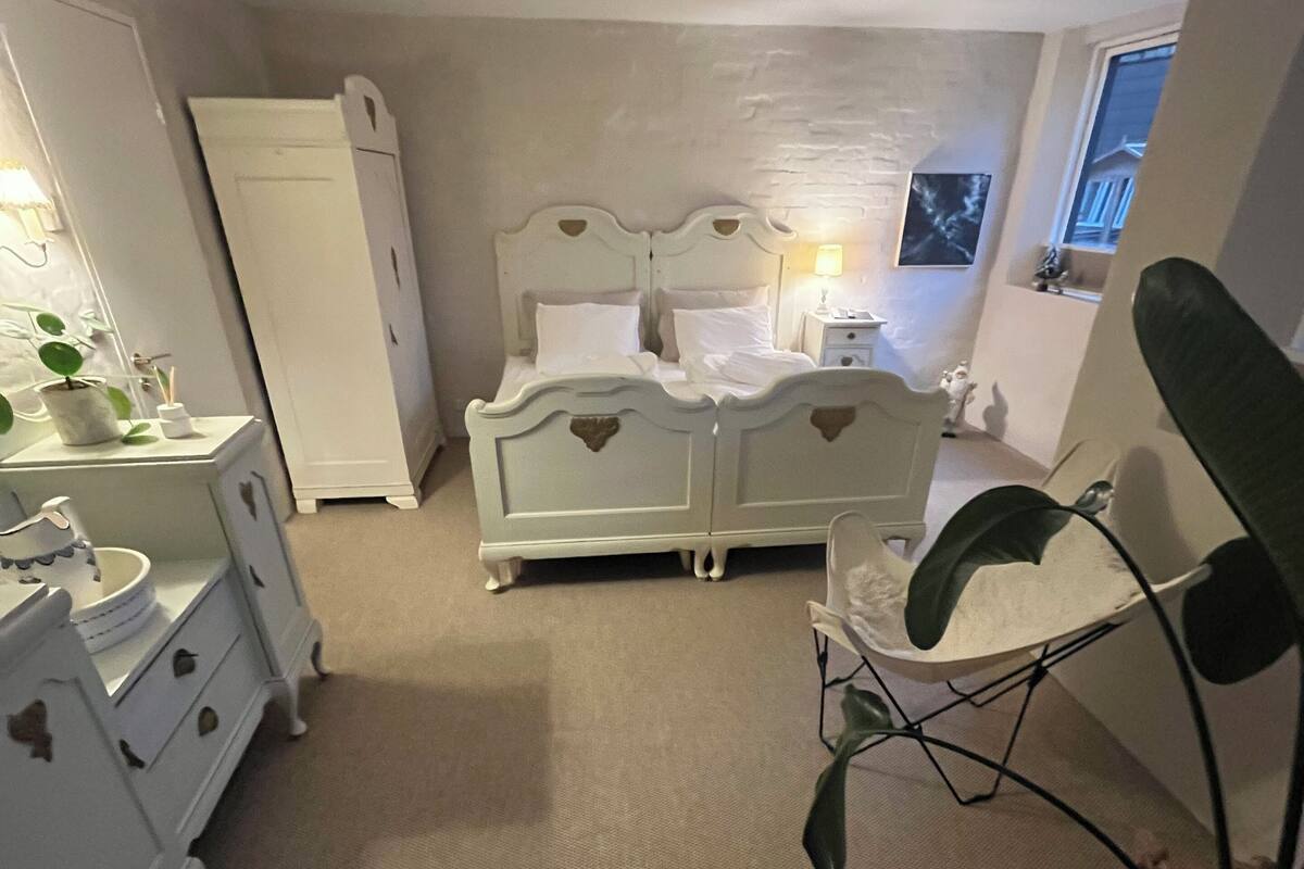A bedroom with a double bed, a nightstand, a dresser, and a plant.