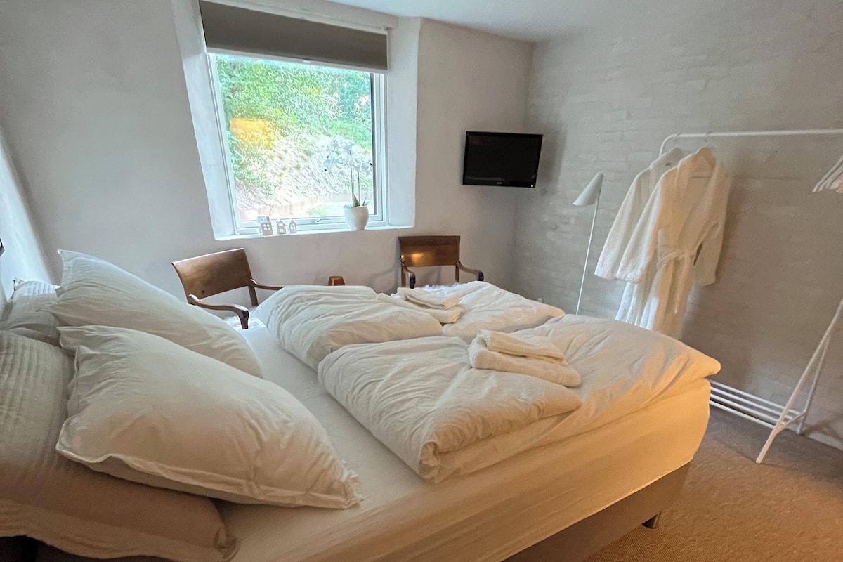 A room with a bed, a window, a TV, and a towel rack.