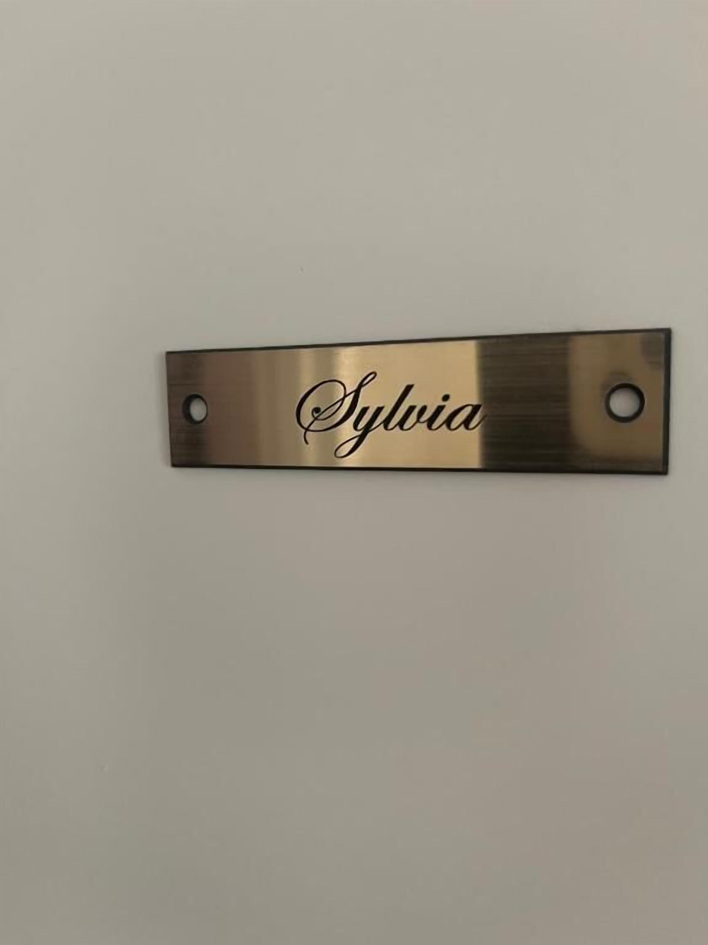 A metallic nameplate with the name "Sylvia" mounted on a wall.