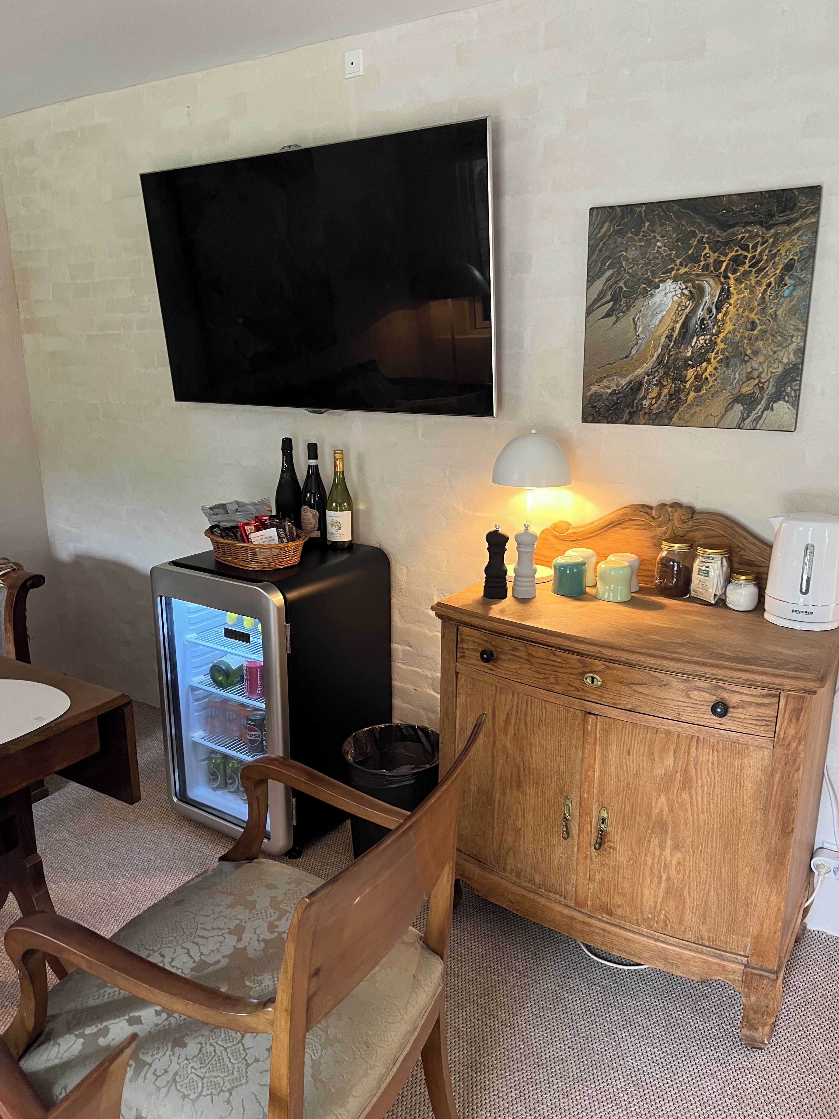 Un espace de vie compact comprenant un téléviseur à écran plat, un réfrigérateur, un meuble en bois et un coin repas avec une chaise et une table.