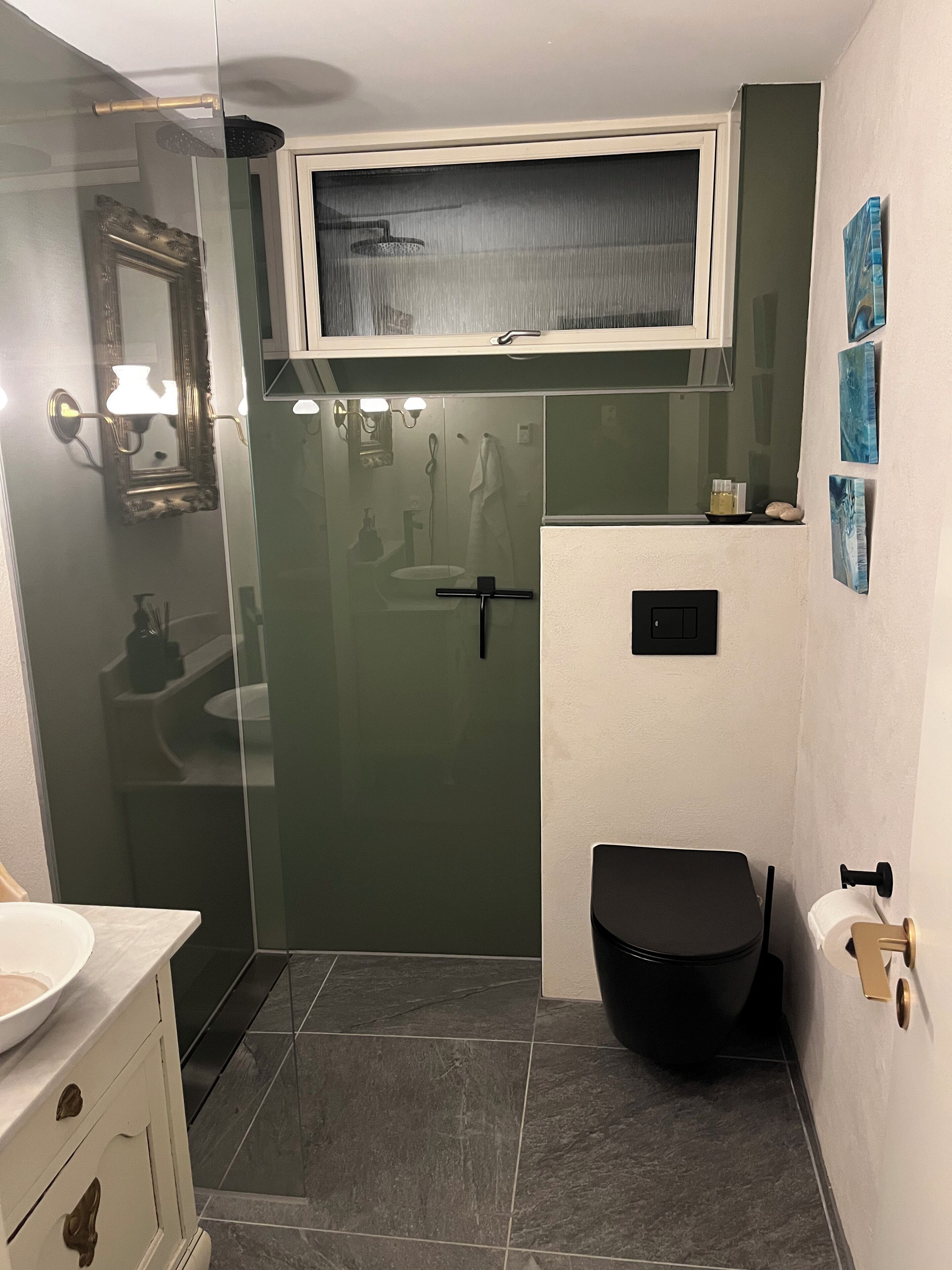 A modern bathroom with a glass shower enclosure, a white sink with a marble countertop, and a black toilet.