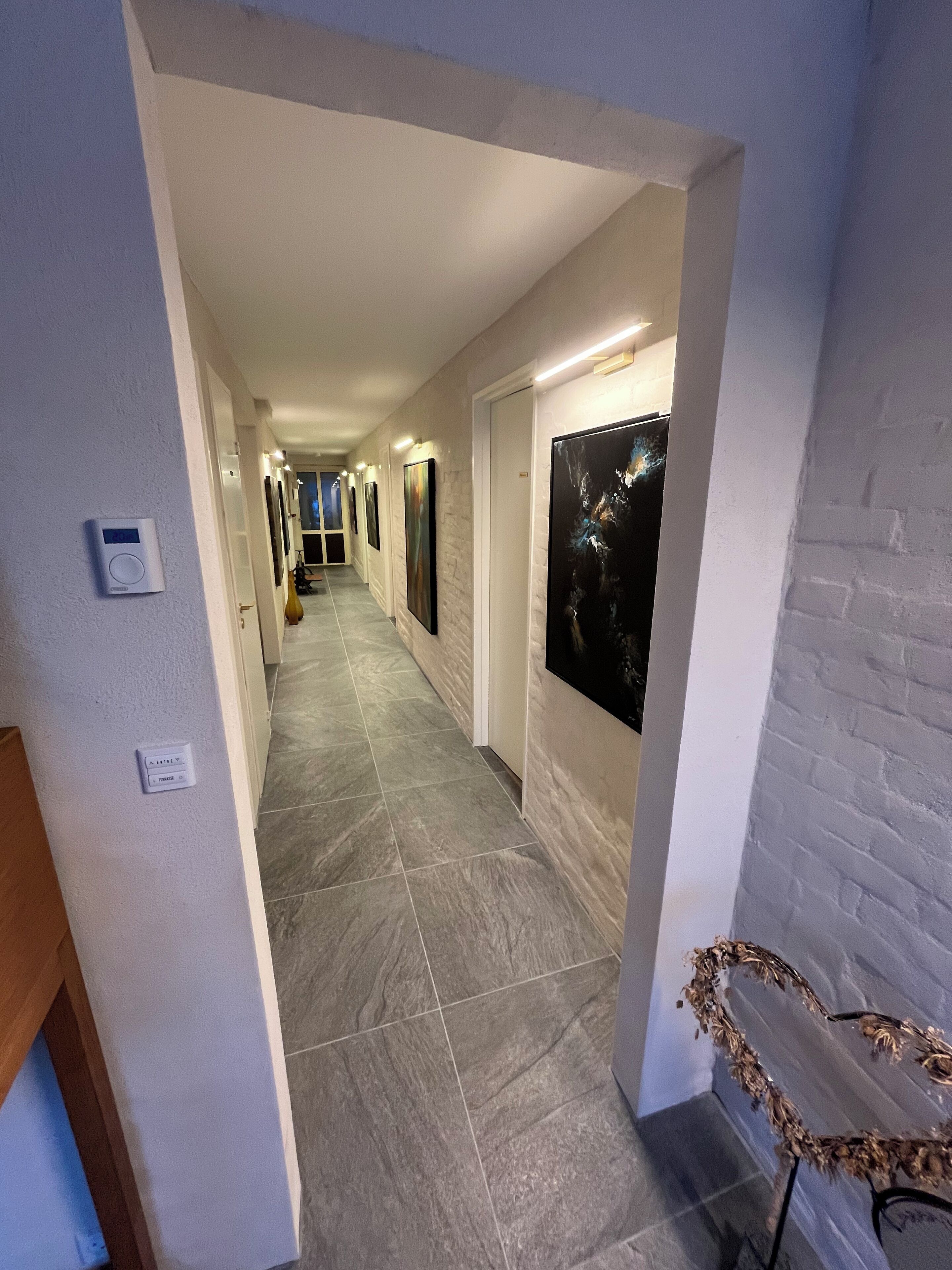 A hallway with grey tiled flooring, white walls, and a door at the end.
