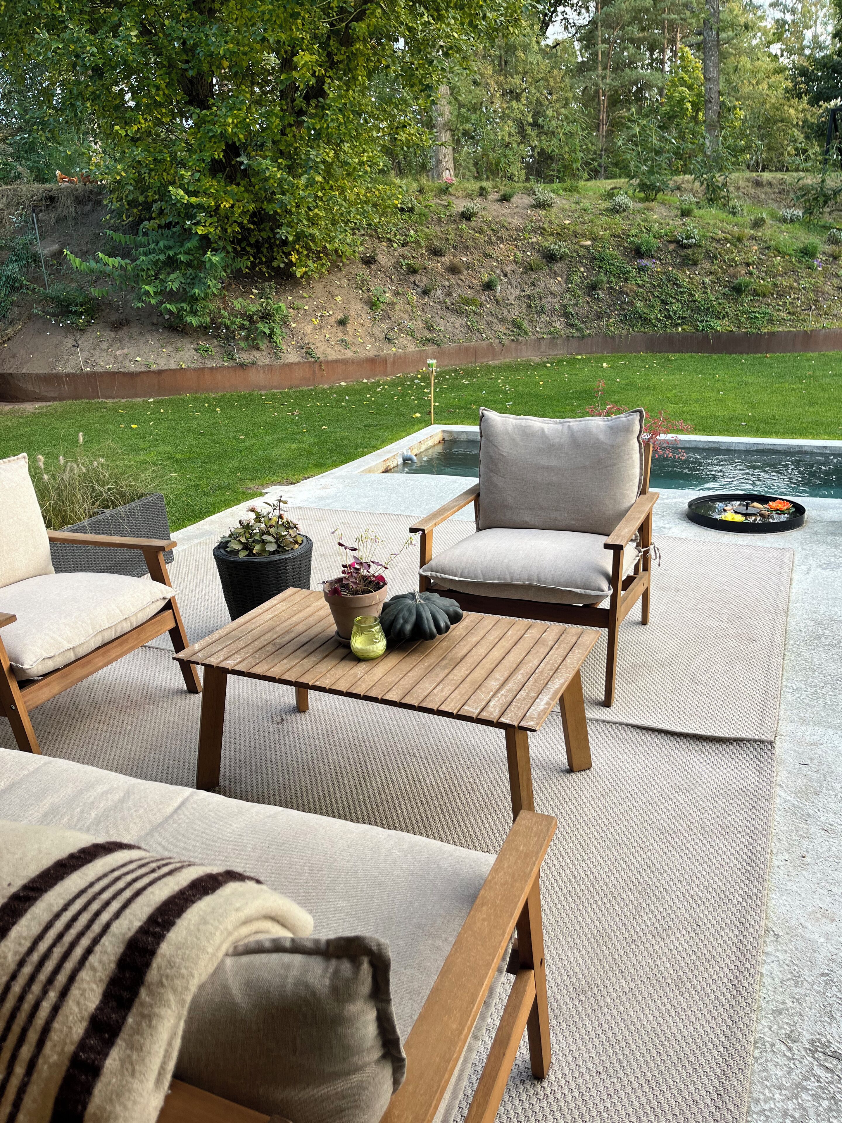 Un espacio al aire libre con mobiliario de madera y una pequeña fuente.