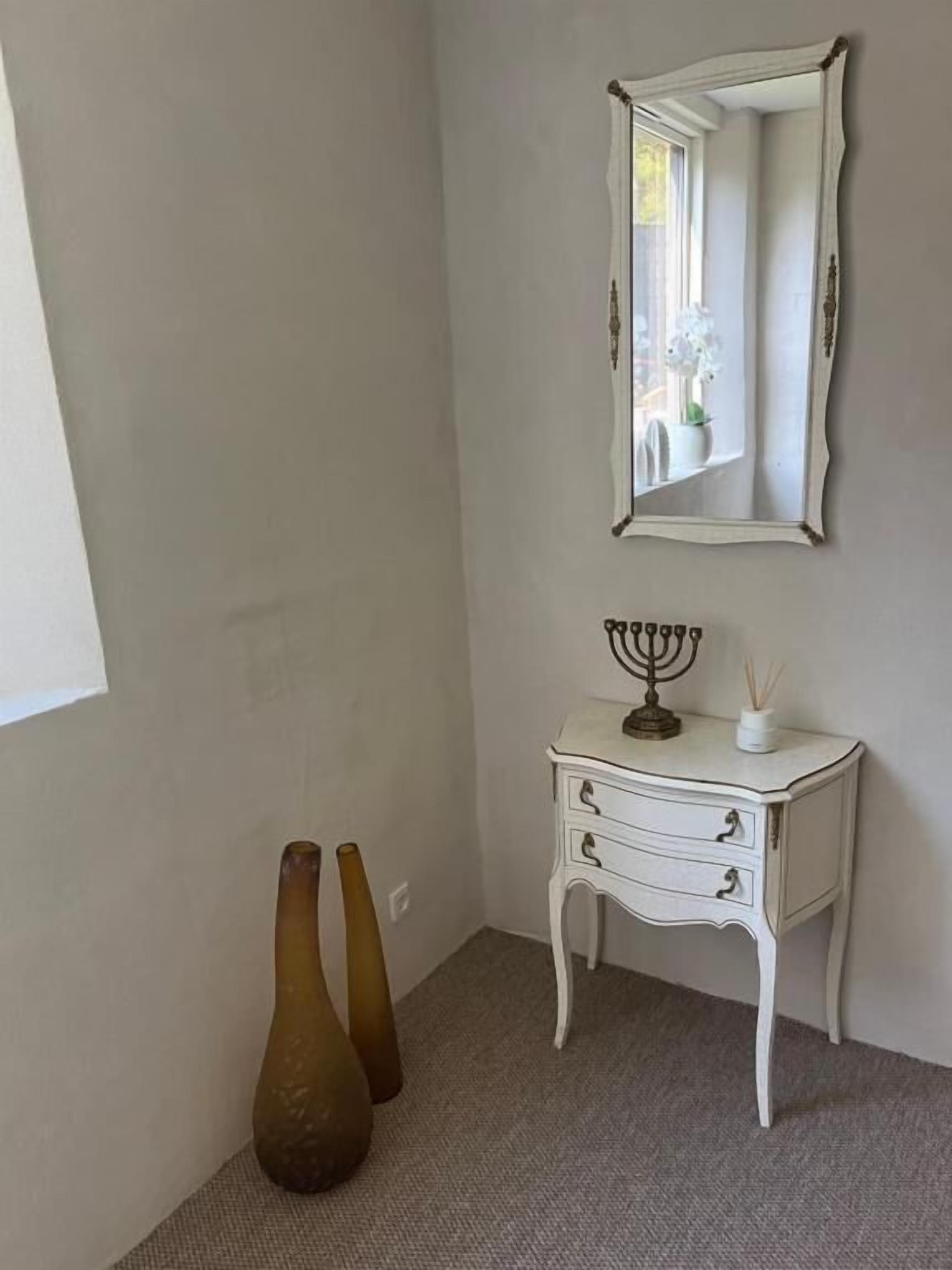 A room with a white dresser, a mirror, and two vases.