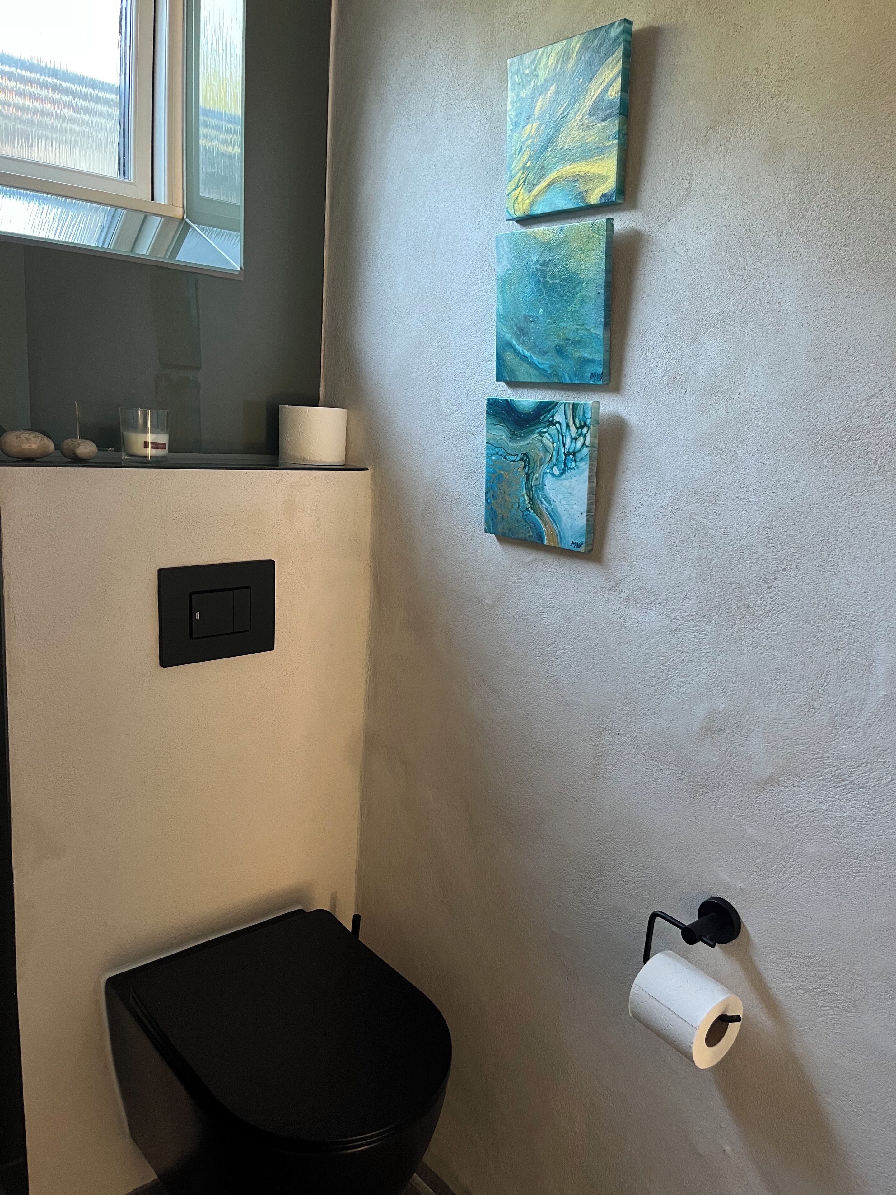 Ein Badezimmer mit Toilette, einem WC-Papierhalter an der Wand und drei abstrakten Bildern.