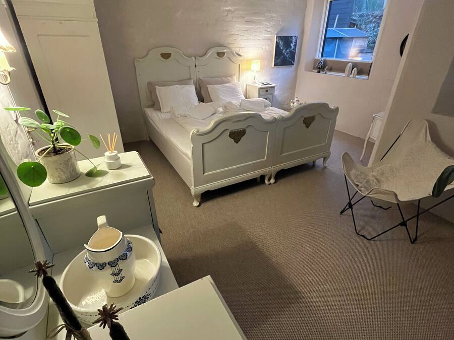 Ein Schlafzimmer mit Bett, Nachttischen, einem Sessel, einer Kommode und einem Fenster.