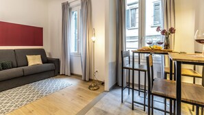 A modern living room with a grey sofa, a dining table with chairs, and a floor lamp. - Wine Apartments Florence Biancone (Florence)