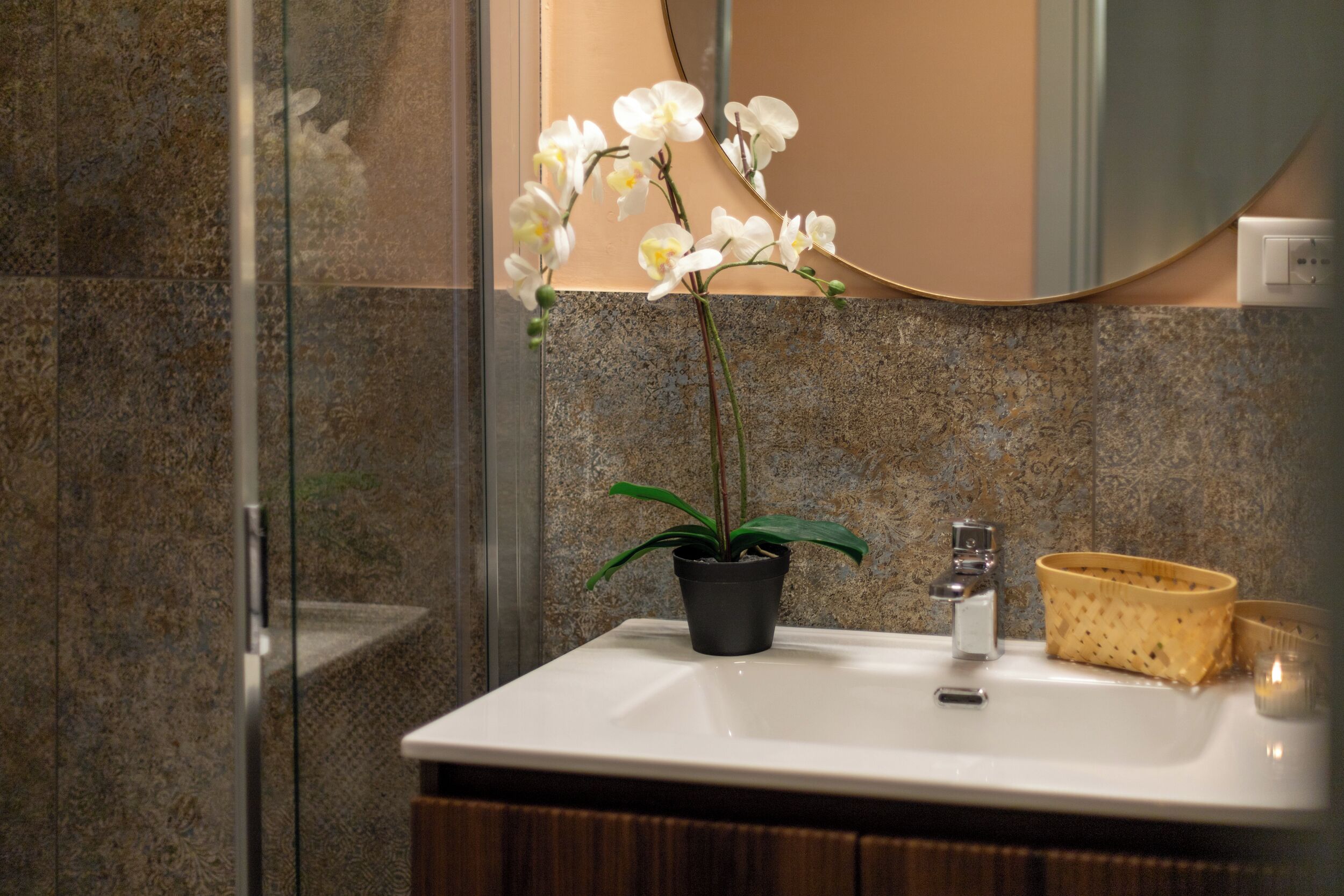 A bathroom with a white sink, a potted orchid, a woven basket, and a mirror.