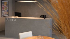Un comptoir d’accueil portant l’inscription « AUREA », au design moderne, une table ronde en bois surmontée d’un vase en verre transparent et, au premier plan, une plante décorative.
