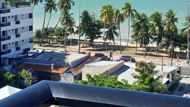 Une vue depuis un balcon donnant sur une plage bordée de palmiers, avec un ciel bleu et dégagé.