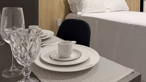 Une chambre d’hôtel avec un lit parfaitement fait, un coin repas avec une table mise pour deux, et une vue dégagée sur le design simple et moderne de la pièce.