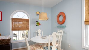 En matplats med ett runt bord, vita stolar, en hängande lampa och dekorativ väggkonst med fiskmotiv.