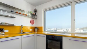 Eine moderne Küche mit weißen Schränken, einer gelben Arbeitsplatte und einem großen Fenster mit Blick auf die Stadt.